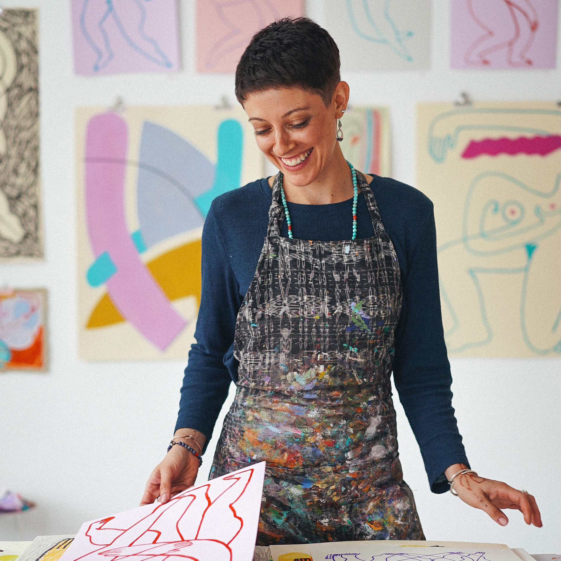 Photograph of a smiling woman standing in a print studio surrounded by colorful prints